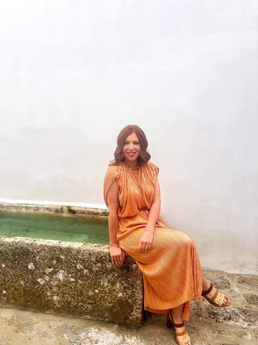 Photo of a woman in an orange dress sitting on a stone pond.