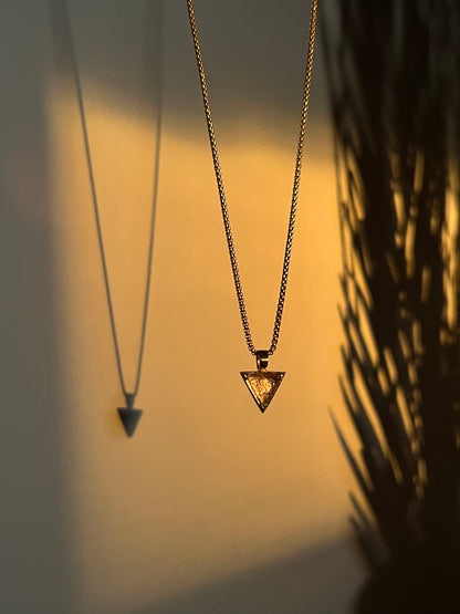 Moody photo of a necklace hanging against a wall with golden sunlight shining on the pendant.