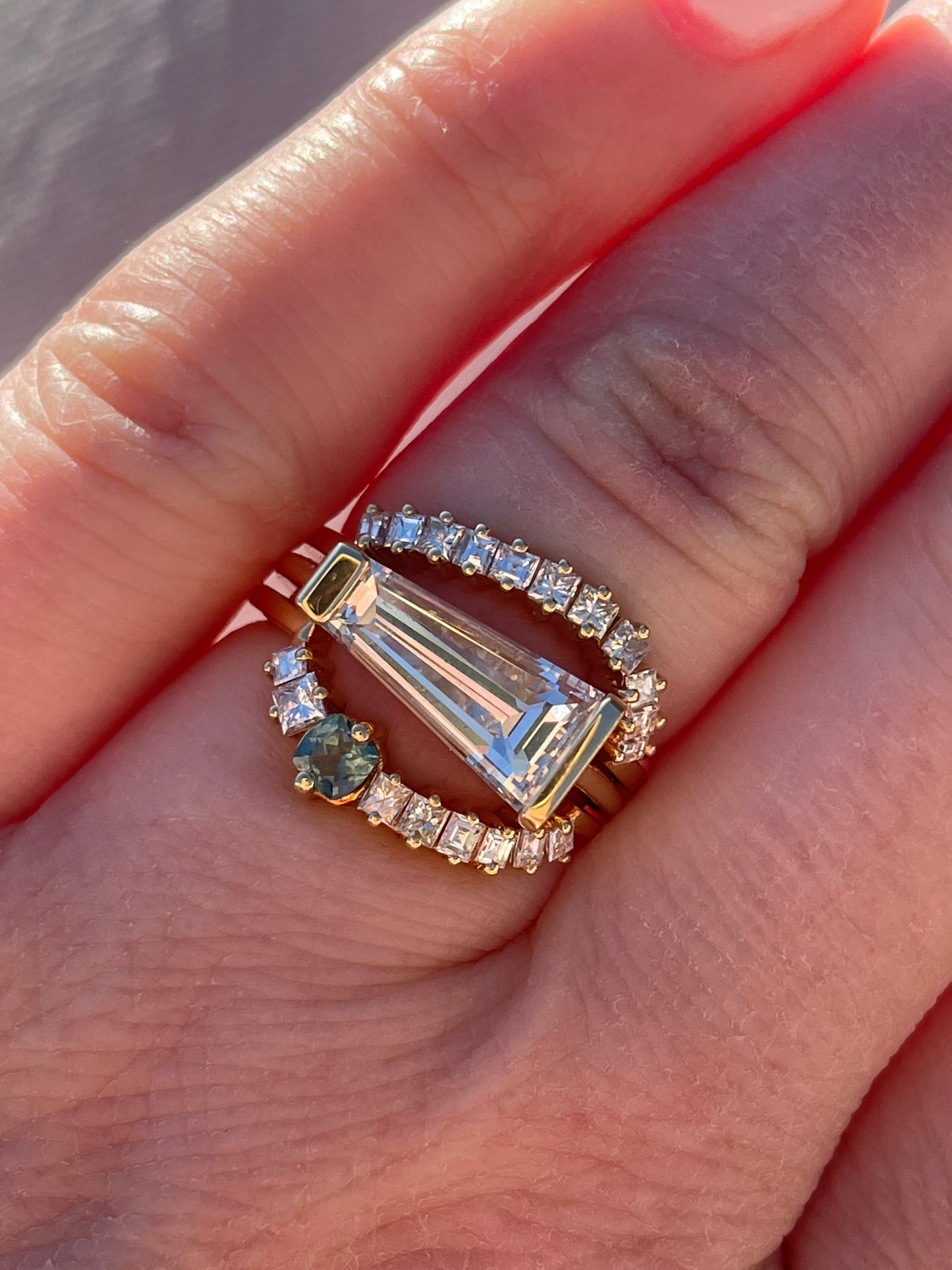 closeup of tapered baguette diamond ring with a top and bottom stacking ring on a women's hand.