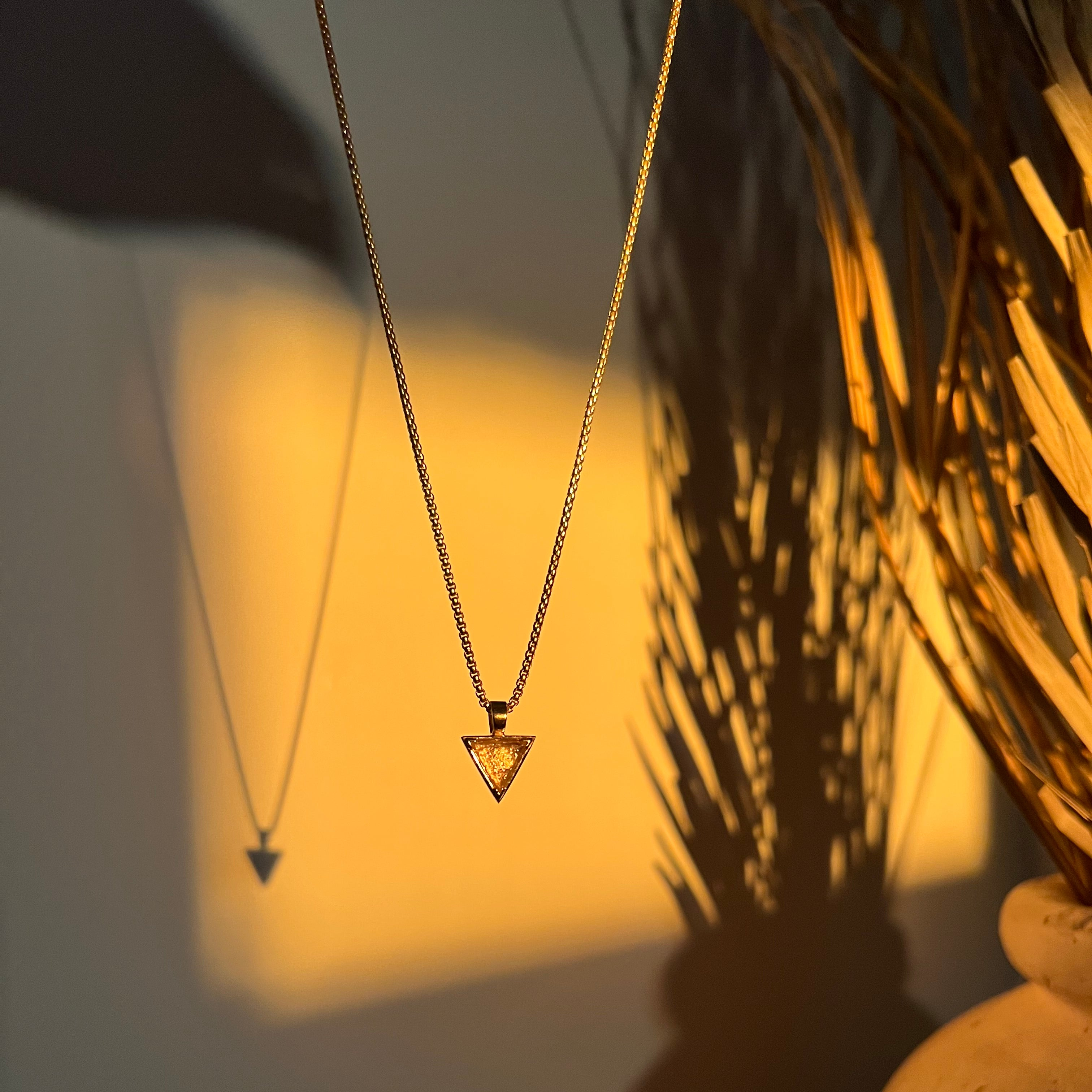 Moody photo of a necklace hanging against a wall with golden sunlight shining on the pendant.