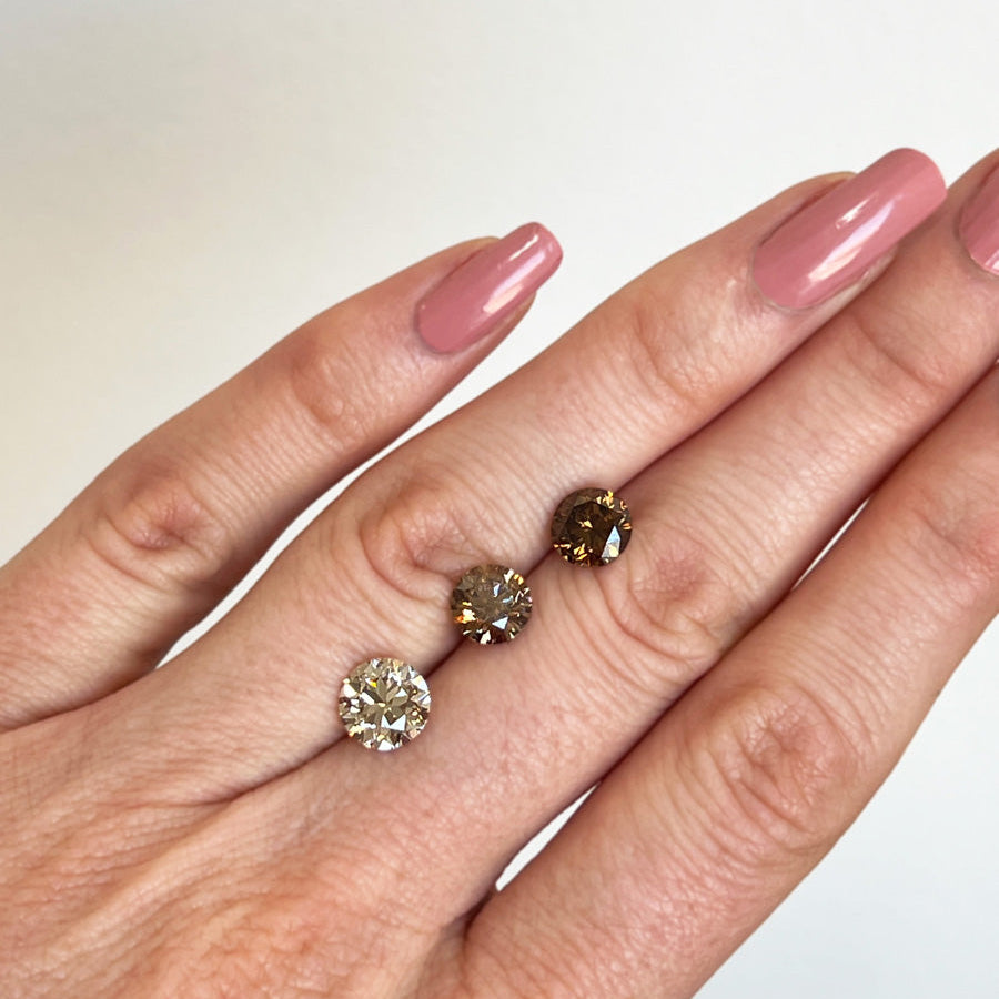 Hand holding two diamond earrings against a neutral background