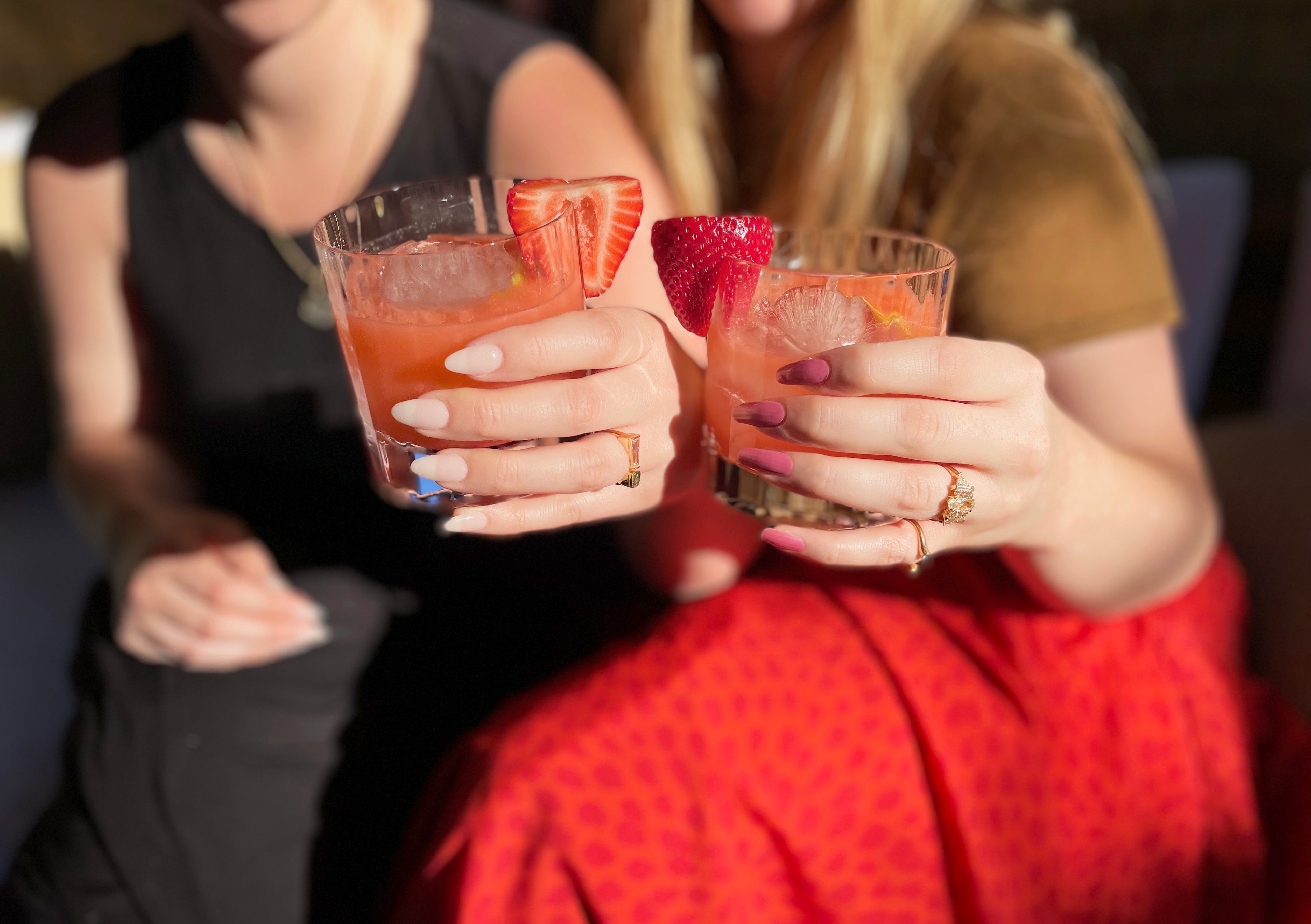 Women's hand holding pink drinks with strawberry garnish featuring beautiful custom rings.