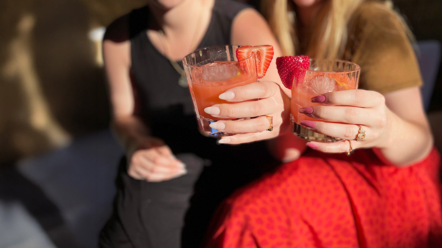 Women's hand holding pink drinks with strawberry garnish featuring beautiful custom rings.