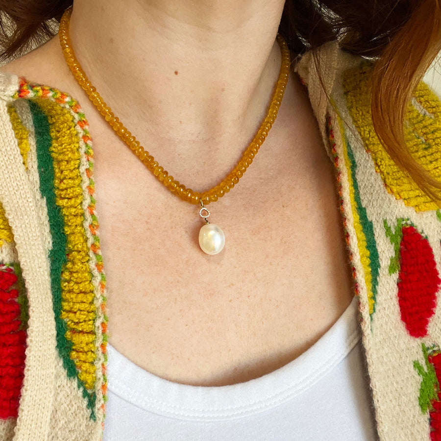 Person wearing a beaded necklace with a pearl pendant, against a colorful background.